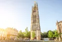 Pey-Berland Tower, a 15th-century Gothic bell tower in Bordeaux, featuring ornate spires and a golden statue on top, surrounded by historic buildings and trees.
