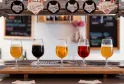 Tasting flight of five craft beers from Burdigala Brewery in Bordeaux, displayed in glasses on a counter with brewery taps in the background.