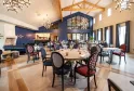 Elegant dining room at Château Fage La Maison des Vignes in Bordeaux, featuring round wooden tables, black and red patterned chairs, cathedral ceiling with exposed beams, modern chandelier, and large windows.