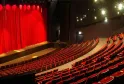 Interior of the National Theatre Bordeaux in Aquitaine showing rows of red seats facing a stage with red curtain and spotlight lighting.