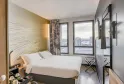 Modern hotel room with double bed with white linens, yellow headboard with wavy patterns, large windows overlooking Bordeaux cityscape, contemporary furnishings and view of the Bassins-à-Flot.