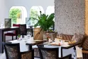 Elegant dining room with set tables, black and gold velvet chairs, arched windows overlooking greenery, floral and minimalist decor.