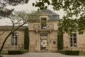 Classical stone mansion facade in Bordeaux with wrought iron balcony, ornate central doorway, cypress trees and manicured landscaping at Cordeillan.