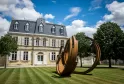 Château Malescasse in Bordeaux featuring classical stone architecture, slate mansard roof, and a contemporary rust-colored metal sculpture on manicured lawns