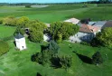 Aerial view of Château Pierre de Montignac, Tanins guesthouse near Bordeaux, featuring a stone manor house, farm buildings, white tower, lush vineyards and rolling countryside landscape