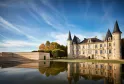 Château Pichon Baron in Bordeaux featuring distinctive conical towers and stone façades, reflected in still water, surrounded by manicured gardens and outbuildings