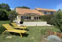 Sunny garden view of Château La Gontrie featuring a yellow lounger, manicured lawn, paved terrace with BBQ, and tile-roofed house in the background.