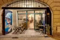 Storefront of Levain Le Vin wine shop in Bordeaux, featuring an outdoor terrace with folding chairs, illuminated display windows and blue promotional poster