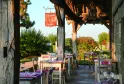 Shaded terrace of La Table du Lavoir in Bordeaux with set tables, purple chairs and red signage, landscaped garden in the background