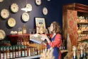 A saleswoman displays products at the Echoppe de la Lune in Bordeaux, surrounded by wine and spirits bottles, with decorative blue and white plates hanging on the wall.