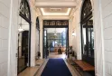 Elegant entrance hallway of a Bordeaux boutique hotel featuring white columns, ornate black doors, coffered ceiling with lighting, and blue carpet leading to the reception area