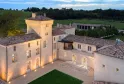 Aerial nighttime view of Château Lafaurie Peyraguey in Bordeaux, illuminated with its distinctive tower, tiled roofs and terraces, surrounded by vineyards.
