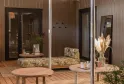 Modern spa interior featuring a suspended woven rattan pendant light, natural wood furniture, black glazed doors, grey panelled walls, decorative plants and wellness elements in a warm ambiance.