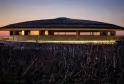 The Dome of Bordeaux glowing at dusk, a modern rounded building in a harvested cornfield with lit windows against a blue and orange twilight sky.